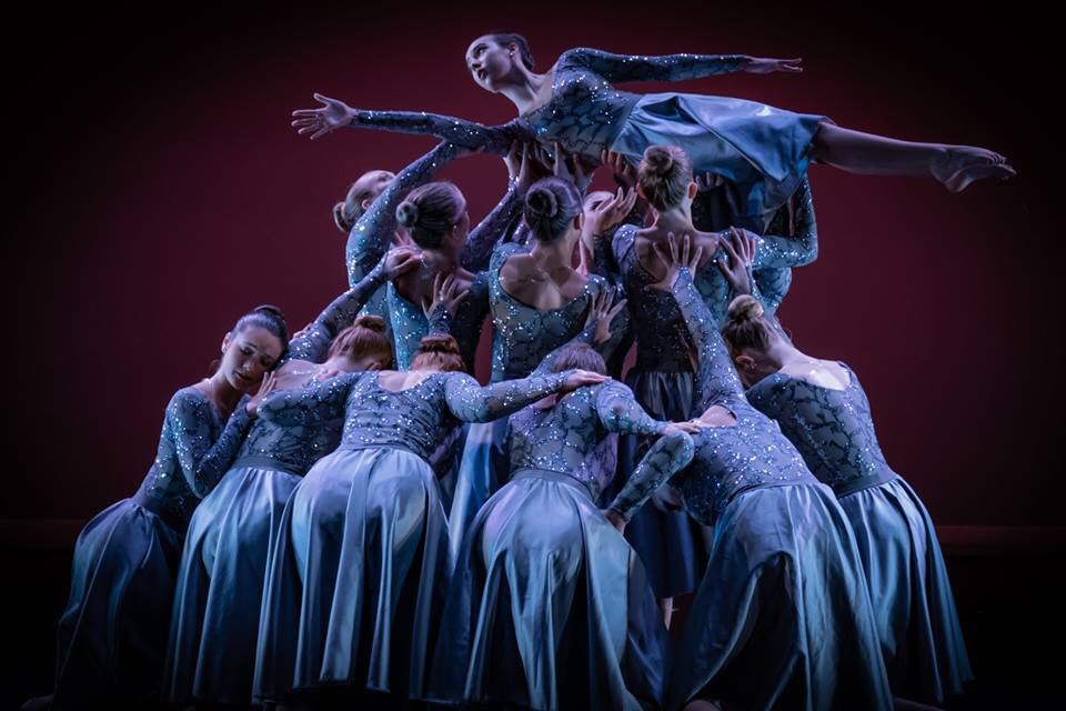 Dance ensemble supporting a lifted performer during a stage performance.